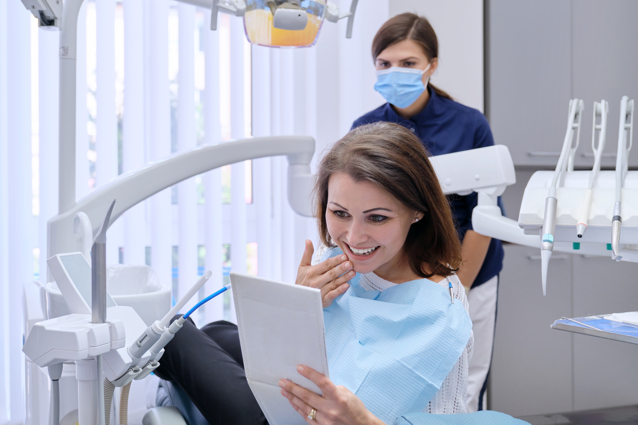 happily surprised female patient looking in a hand mirror at dental office