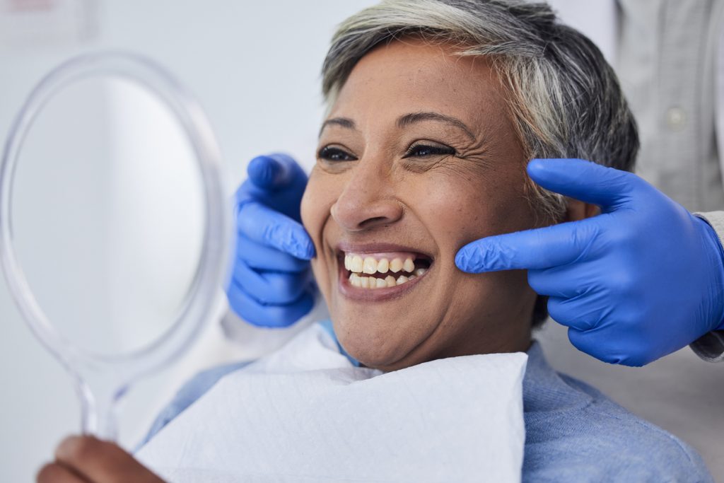 female gum surgery patient smiling with hand mirror