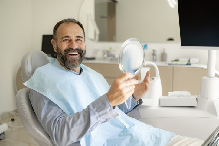 PST patient smiling in the dental chair with a hand mirror